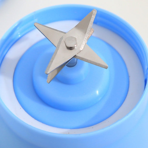 Blue portable electric fruit juicer with metal cross-blade inside clear base cup