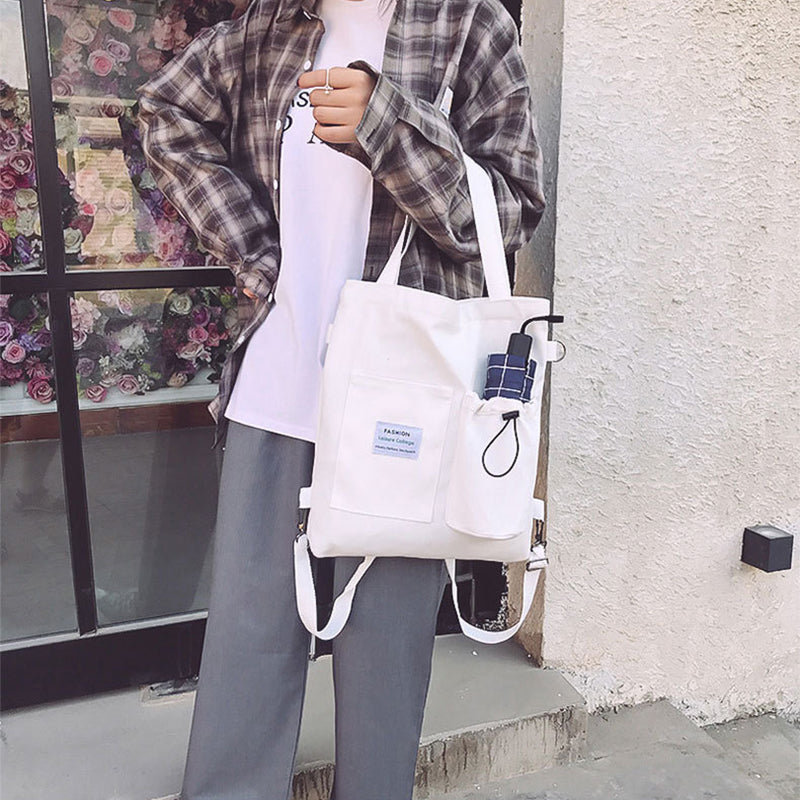 White canvas tote bag with front pocket, drawstring cord, and adjustable straps