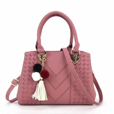 Pink quilt-textured handbag with top handles, crossbody strap, and pom tassel charm