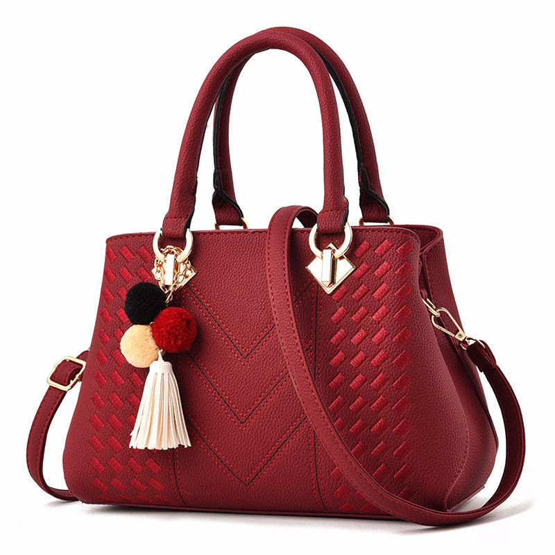 Wine red quilt-textured handbag with top handles, crossbody strap, and pom tassel charm