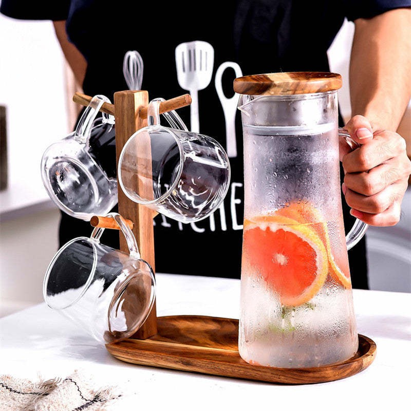 Glass cold water bottle on wood stand, metal lid, citrus slices, person holding handle