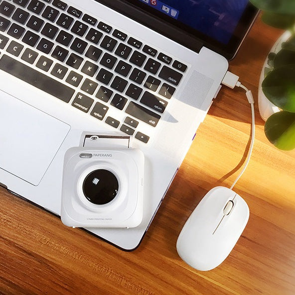 White mini mobile thermal photo printer on desk, front lens facing camera