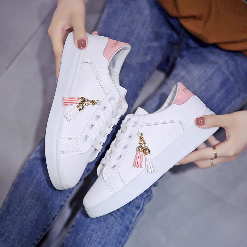 White low-top sneakers with pink inserts and tassel charm, lace-up.