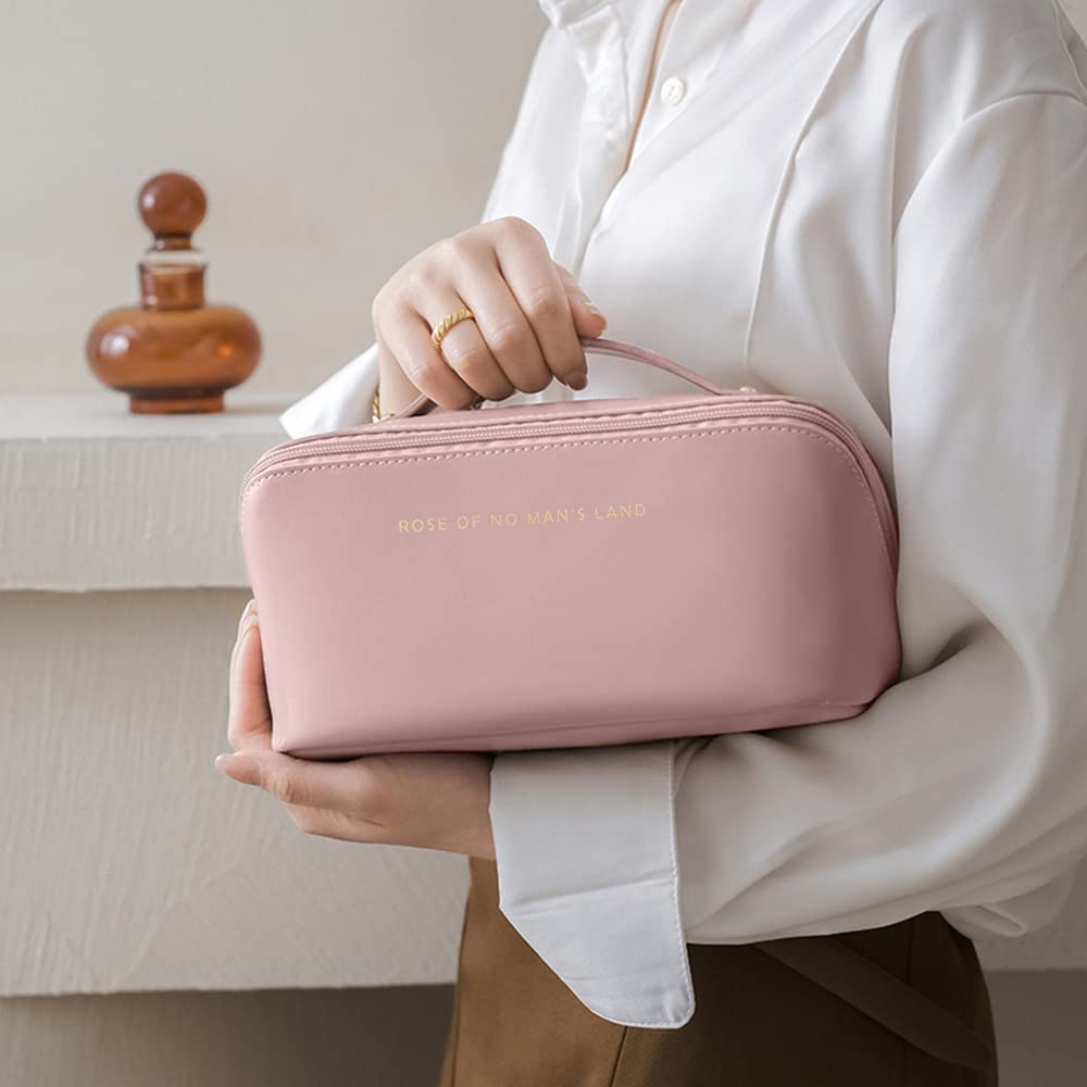 Pink cosmetic bag held by hand with top handle and centered logo text
