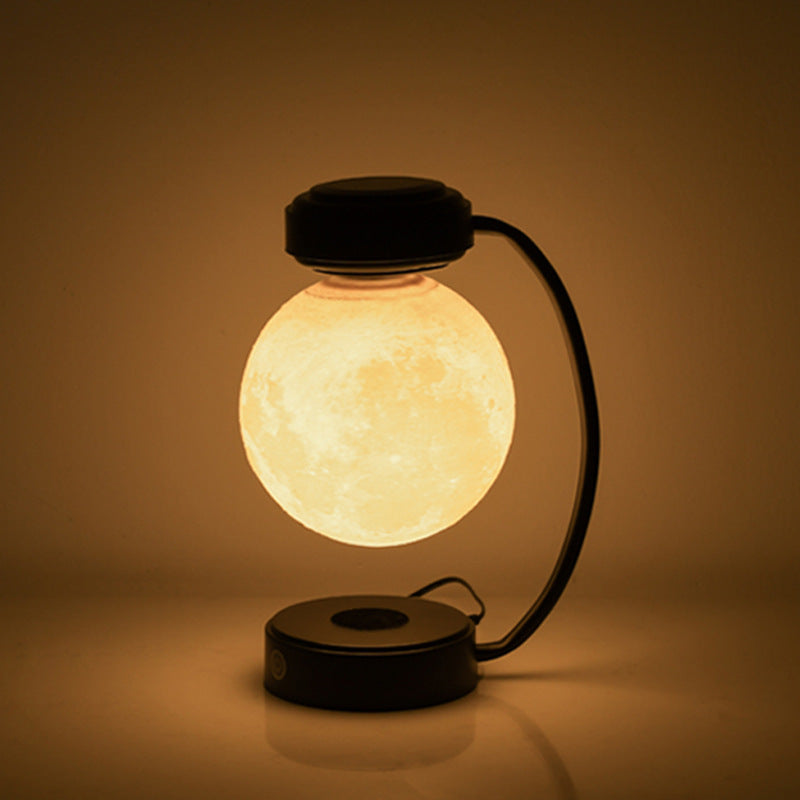 Black moon LED night light with warm glowing floating globe and curved base stand