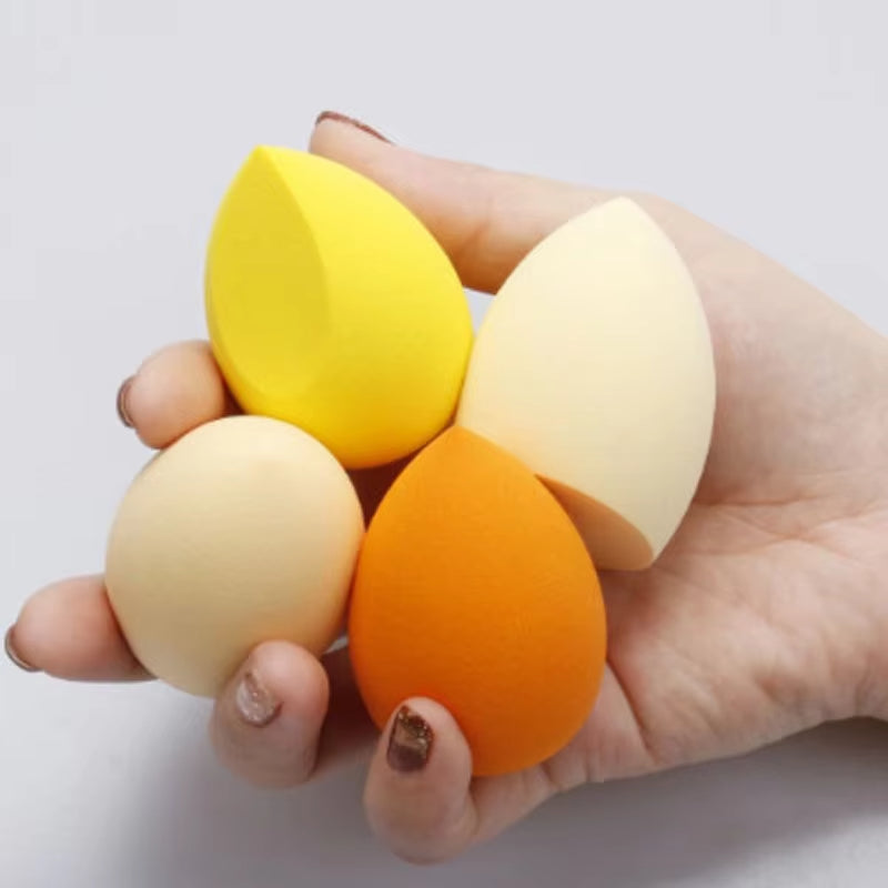 Teardrop makeup sponges in yellow, cream, and orange tones, held in hand