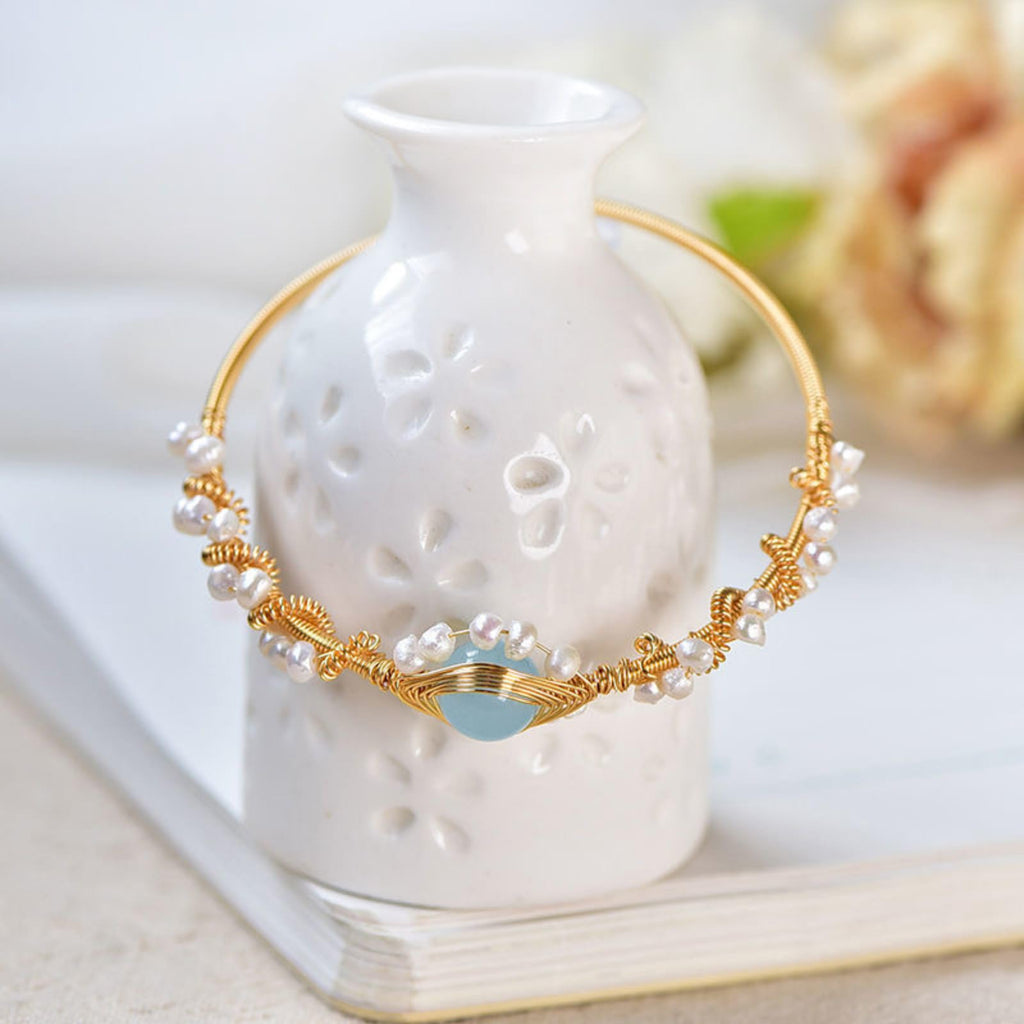 Gold pearl cuff bracelet with blue oval charm and white pearl accents on display