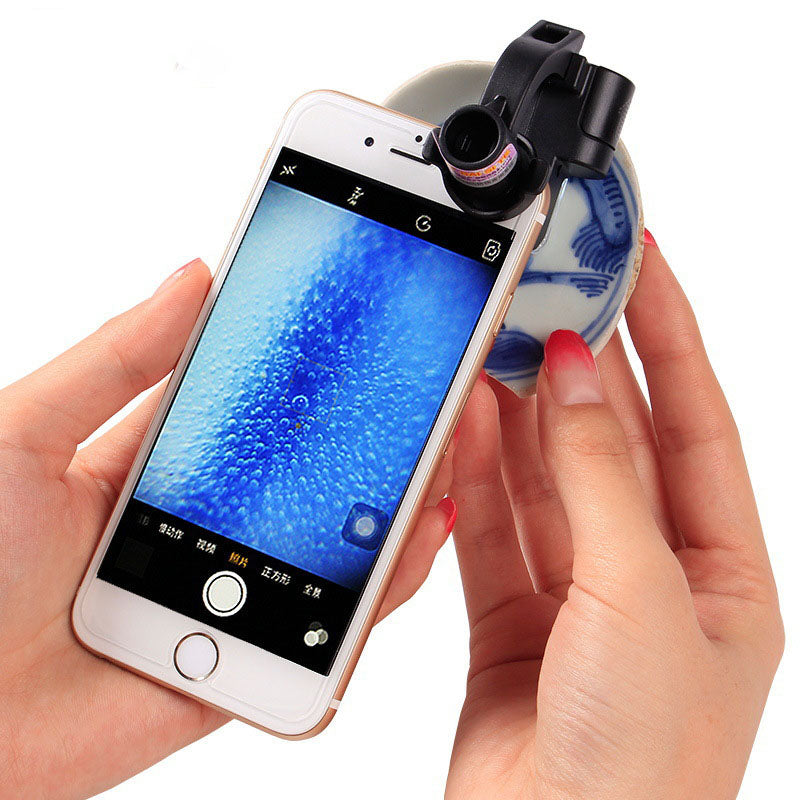 Black clip-on magnifying lens with LED light clipped to a smartphone held in hands