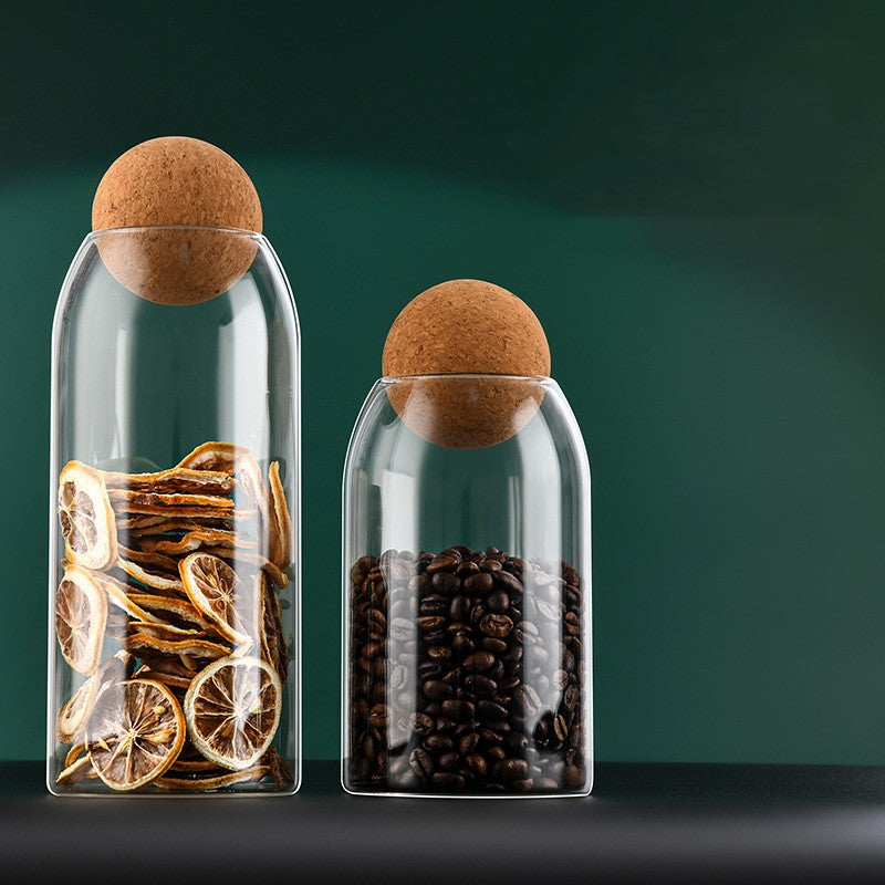 Two clear glass display bottles with cork stoppers; left dried citrus, right coffee beans