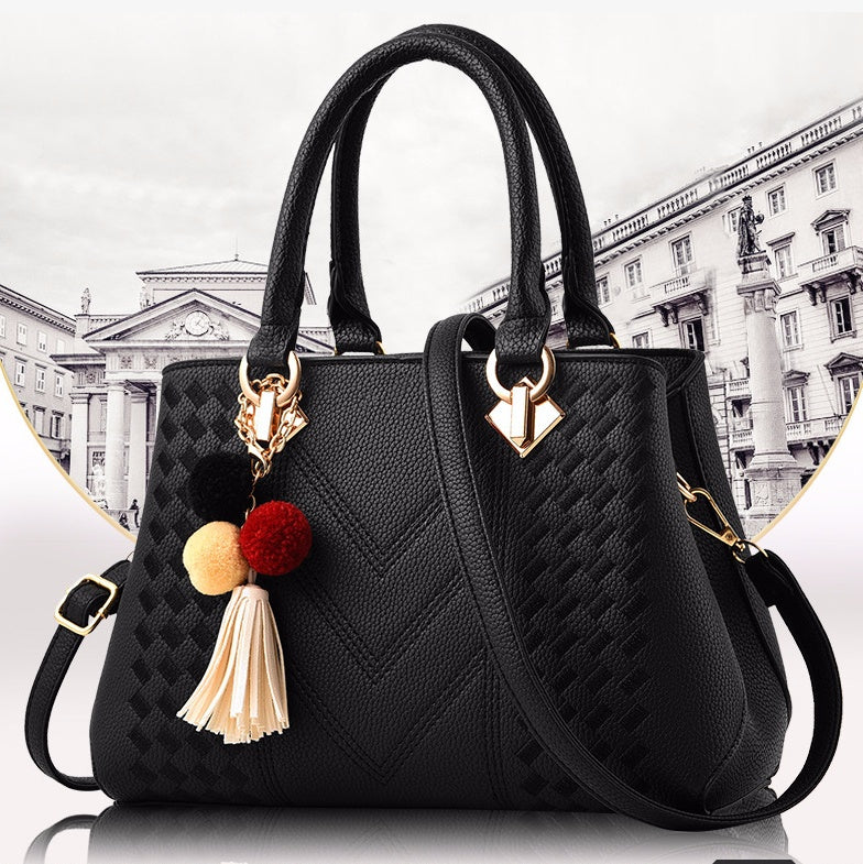 Black quilt-textured handbag with top handles, crossbody strap, and tassel pom charm